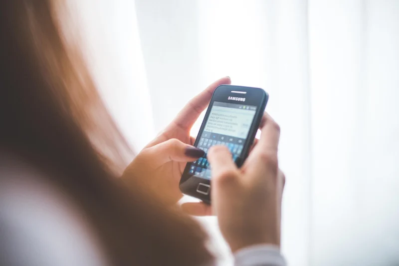 Devojka sedi u polumraku i koristi pametni telefon dok kuca poruke