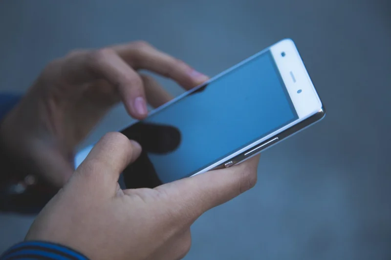 Osoba drži pametni telefon blizu lica u večernjim satima, svetlo ekrana osvetljava mračni prostor