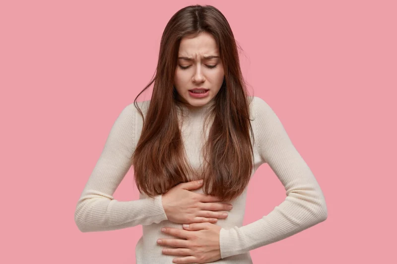Mlada žena drži ruke na stomaku i karlici sa bolnim izrazom lica zbog menstrualnih bolova